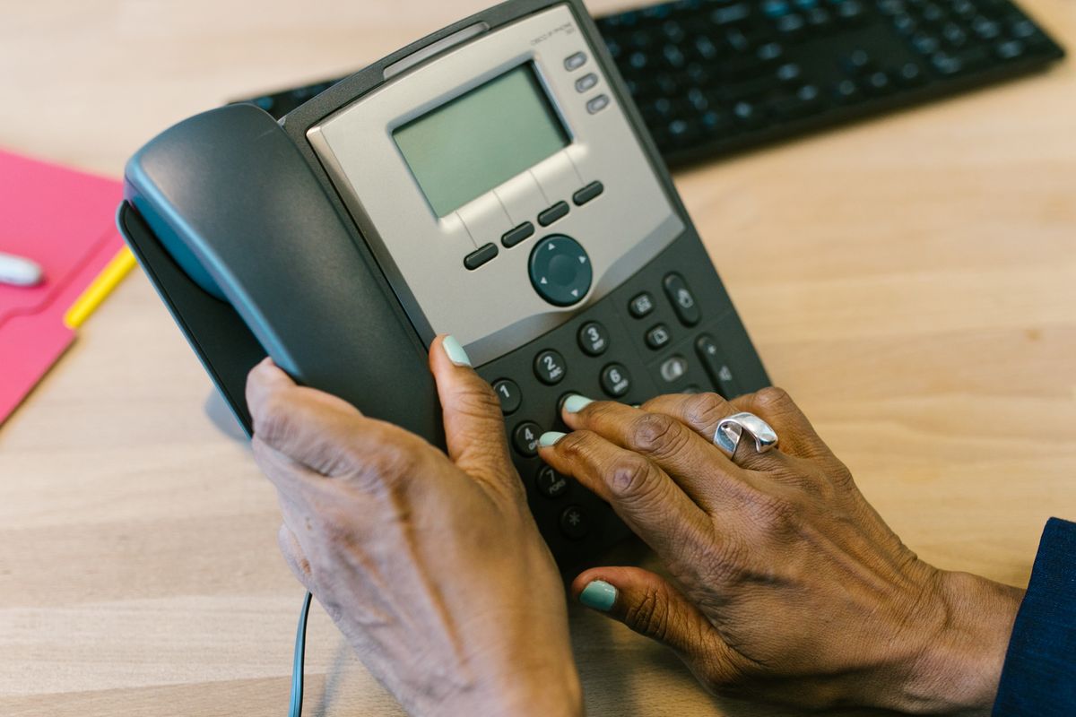 Hands dialing an office desk telephone