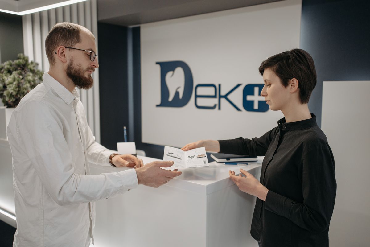 Two people exchanging paperwork at a dental clinic front desk